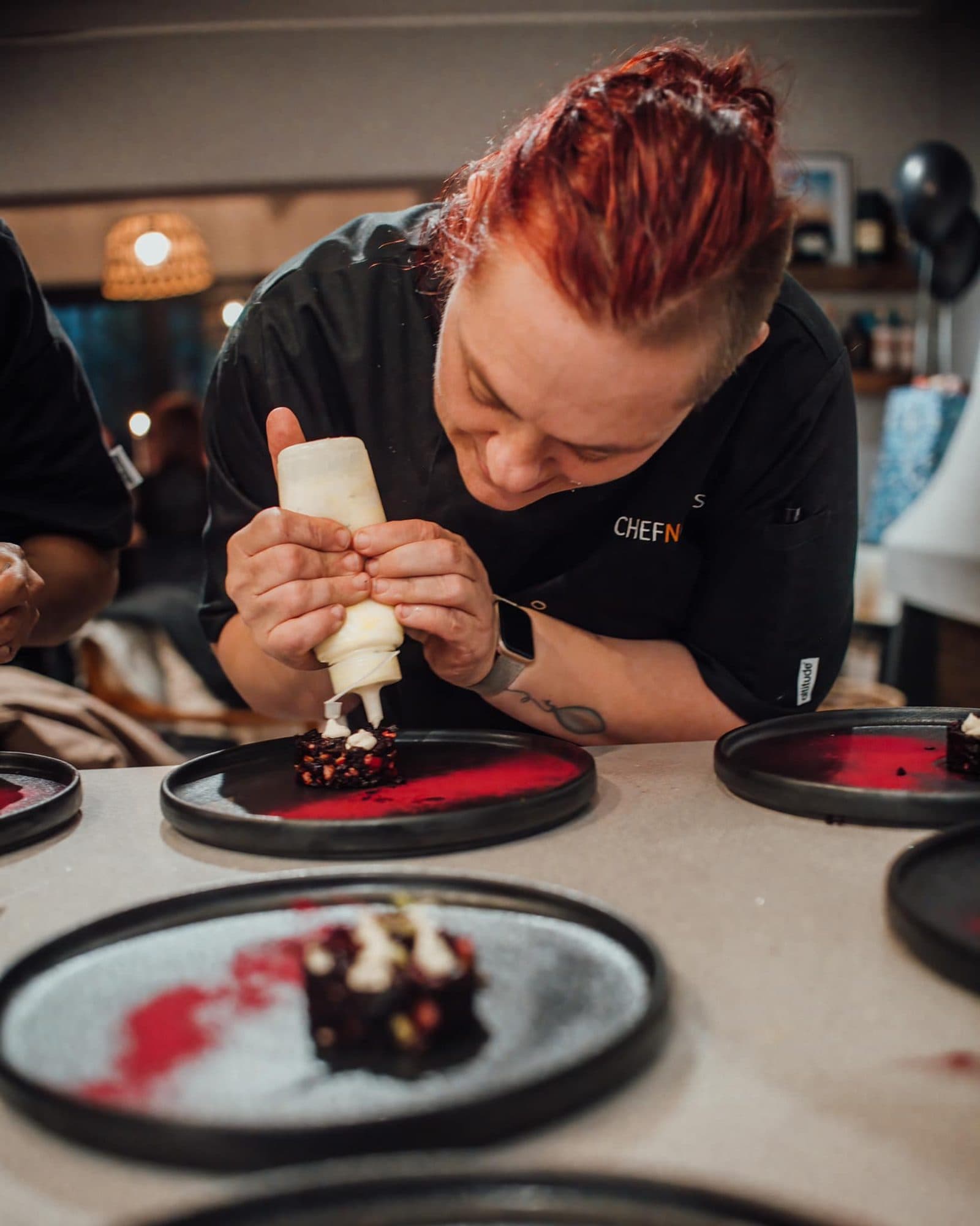 Chef Maradine piping a dessert onto dark plates with concentration