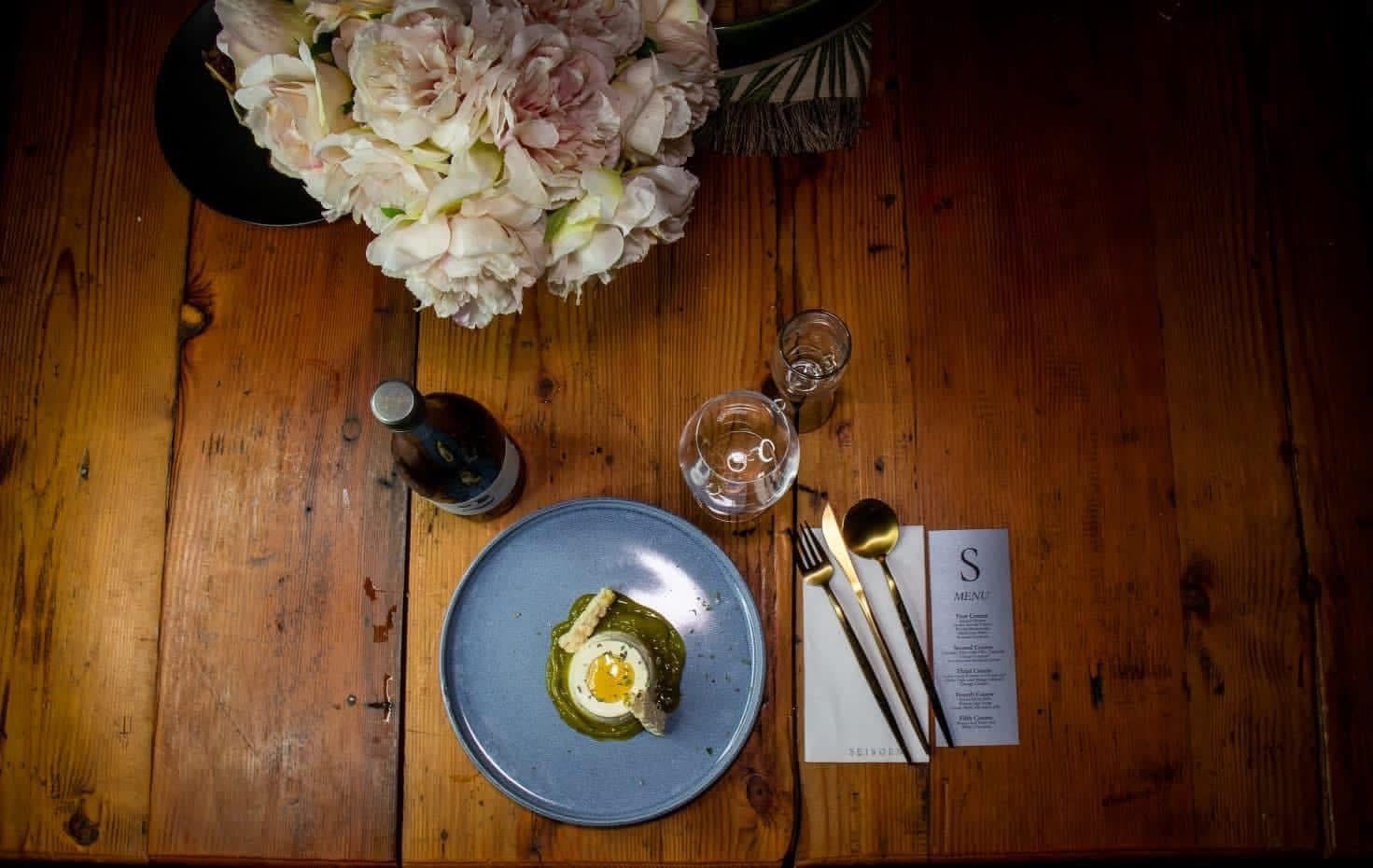 Overhead view of a single plated course on a candlelit wooden table with flowers and a menu card