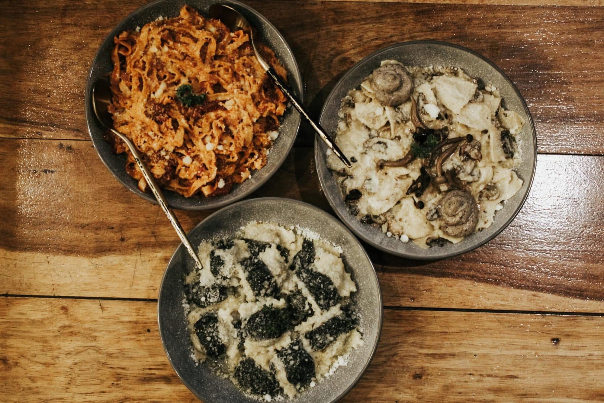 Three bowls of handmade pasta on a rustic wooden table